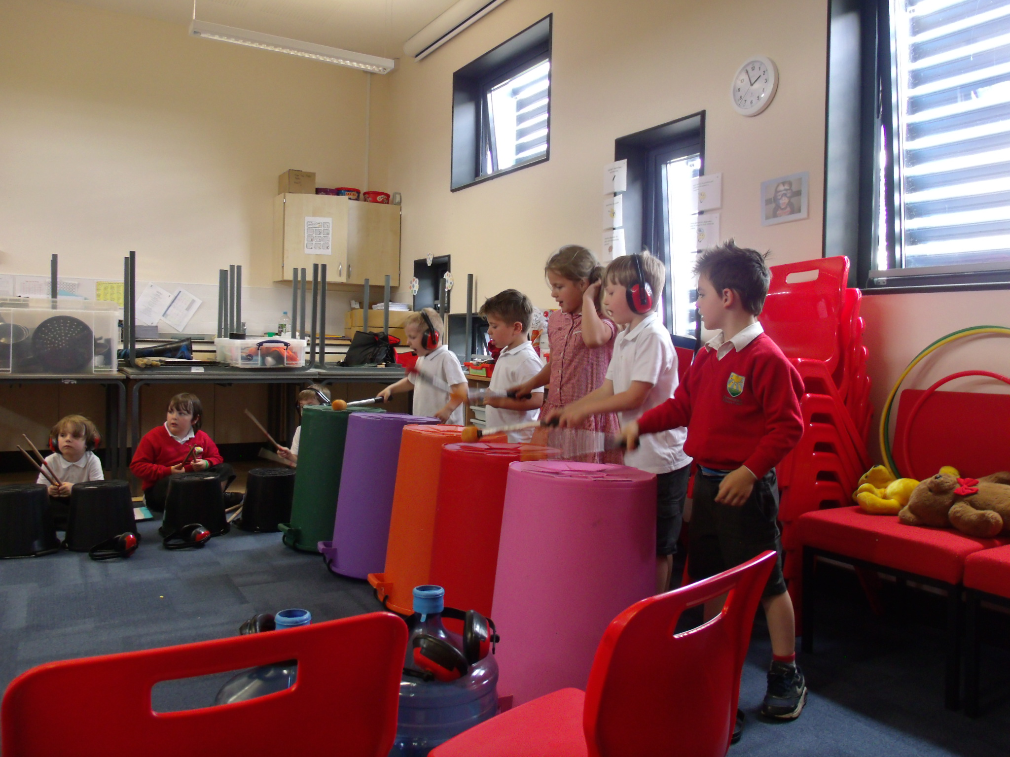 School children playing music on large colourful empty bins