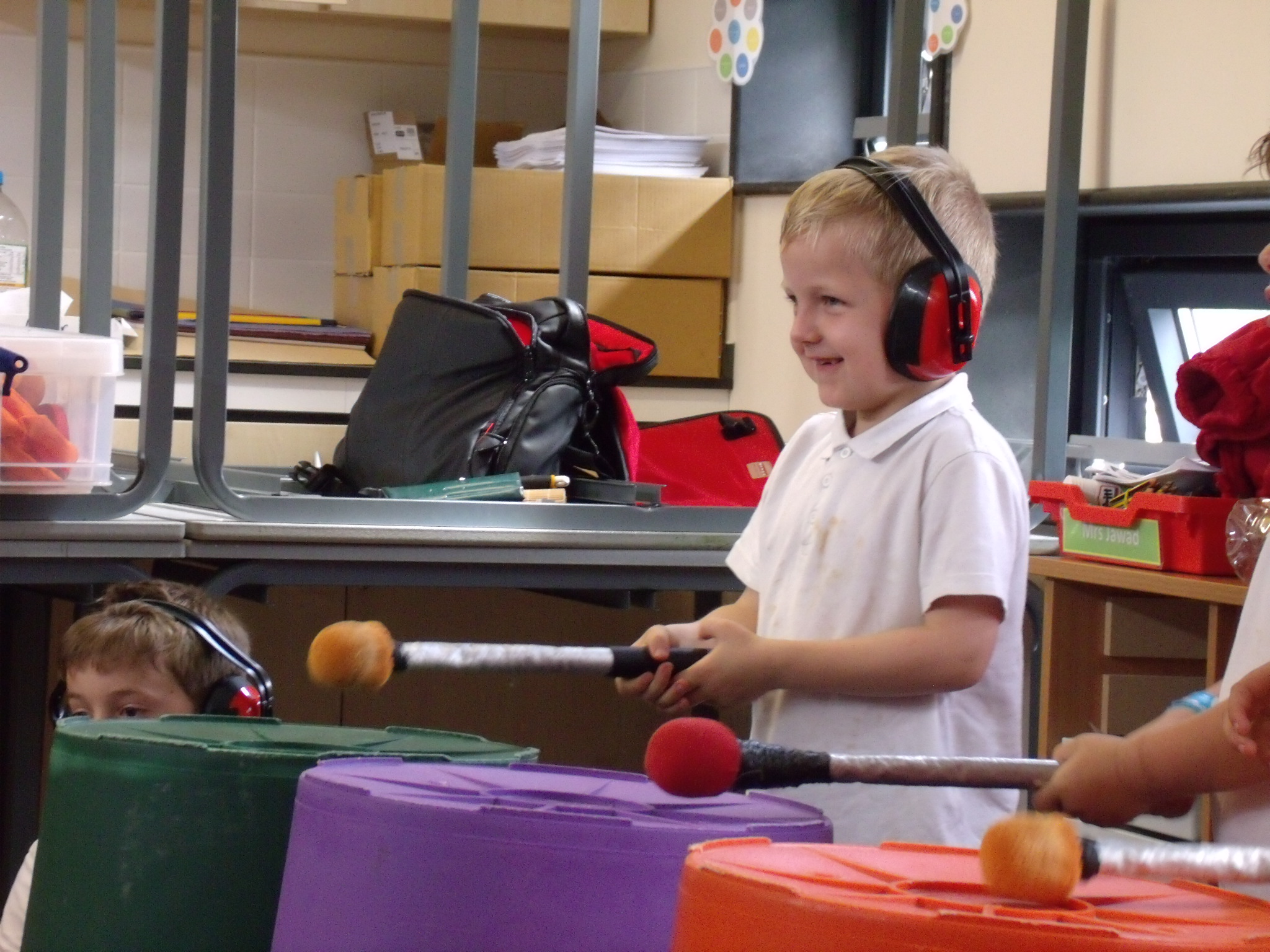 School children playing music on large colourful empty bins